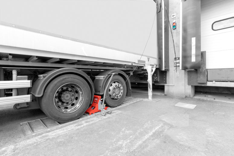 Radkeil POWERCHOCK vor dem Hinterrad des Anhängers, um das Fahrzeug an der Laderampe zu sichern